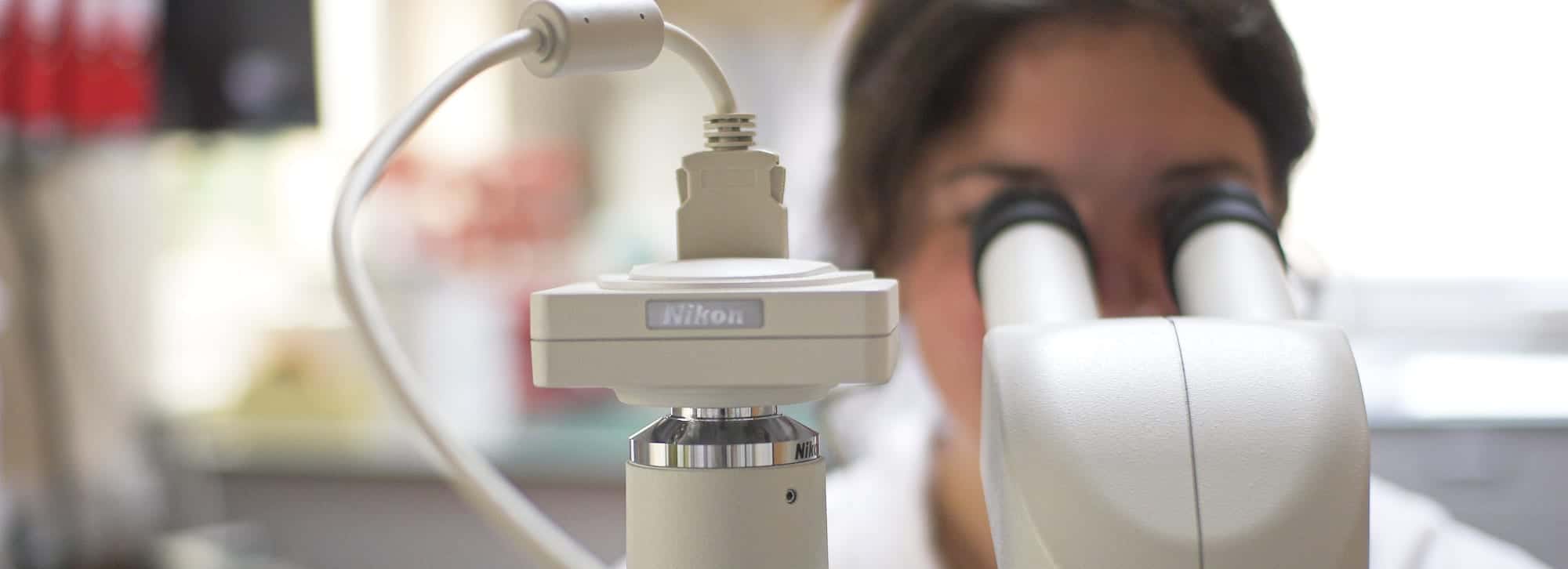 Lab technician looking through microscope lens